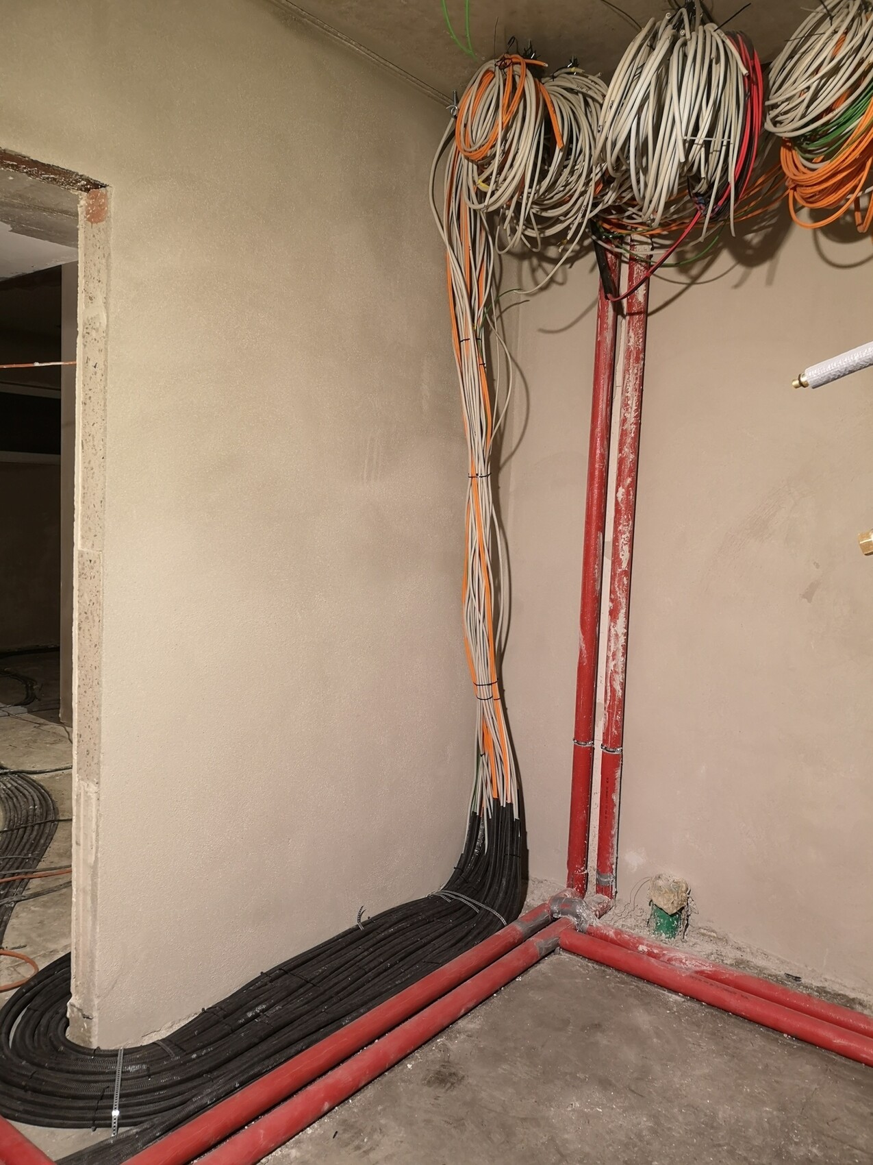 Construction site: cable bundle from the ceiling, red pipes on the wall, black cable on the floor.