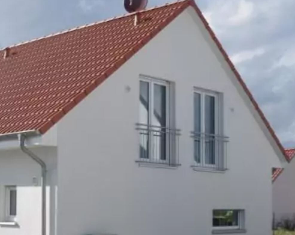 White house with red tile roof, two upper windows with railings.