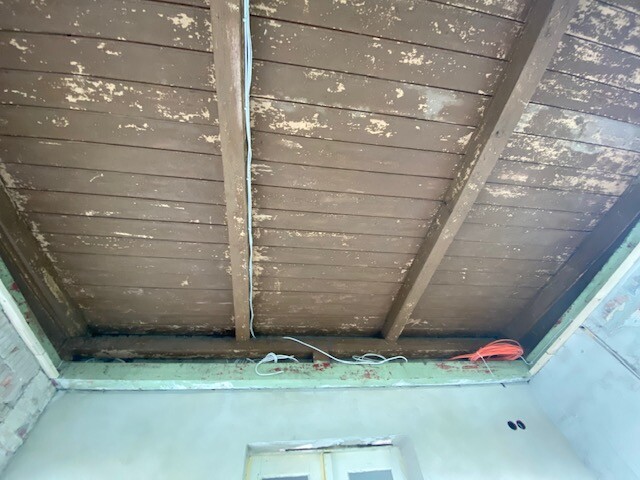 Unfinished room ceiling with wooden beams, plaster chipping, and loose cables along the ceiling molding.