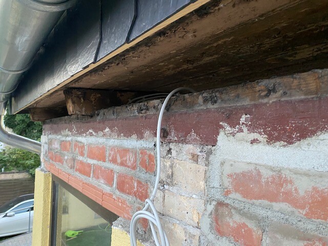 Exterior wall made of brick with wooden beams under the roof, loose grey cables hanging down