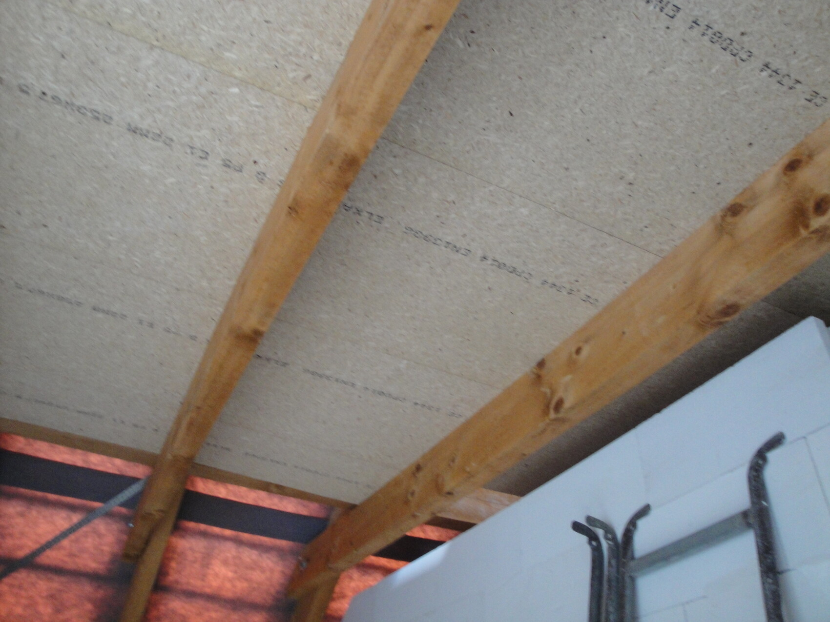 Rohbau-Decke mit Holzbalken und sichtbarer Dämmung zwischen Balken