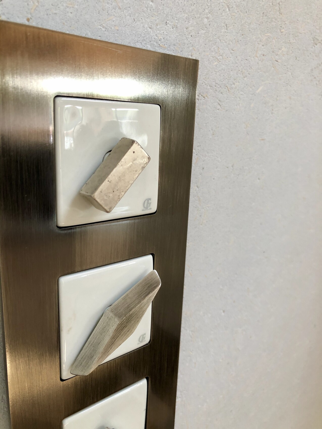 Three white, square light switches in a bronzed metal frame wall plate.