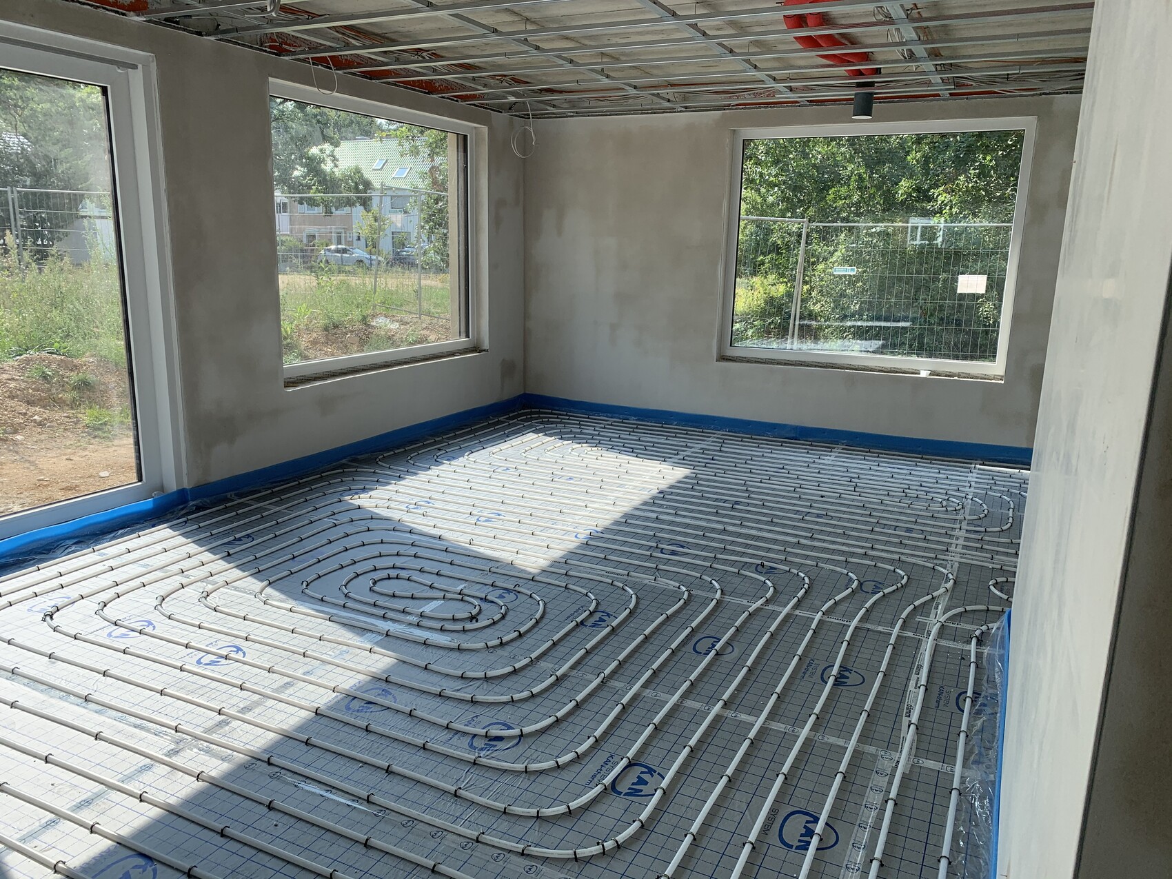 Room under construction with visible underfloor heating and large windows