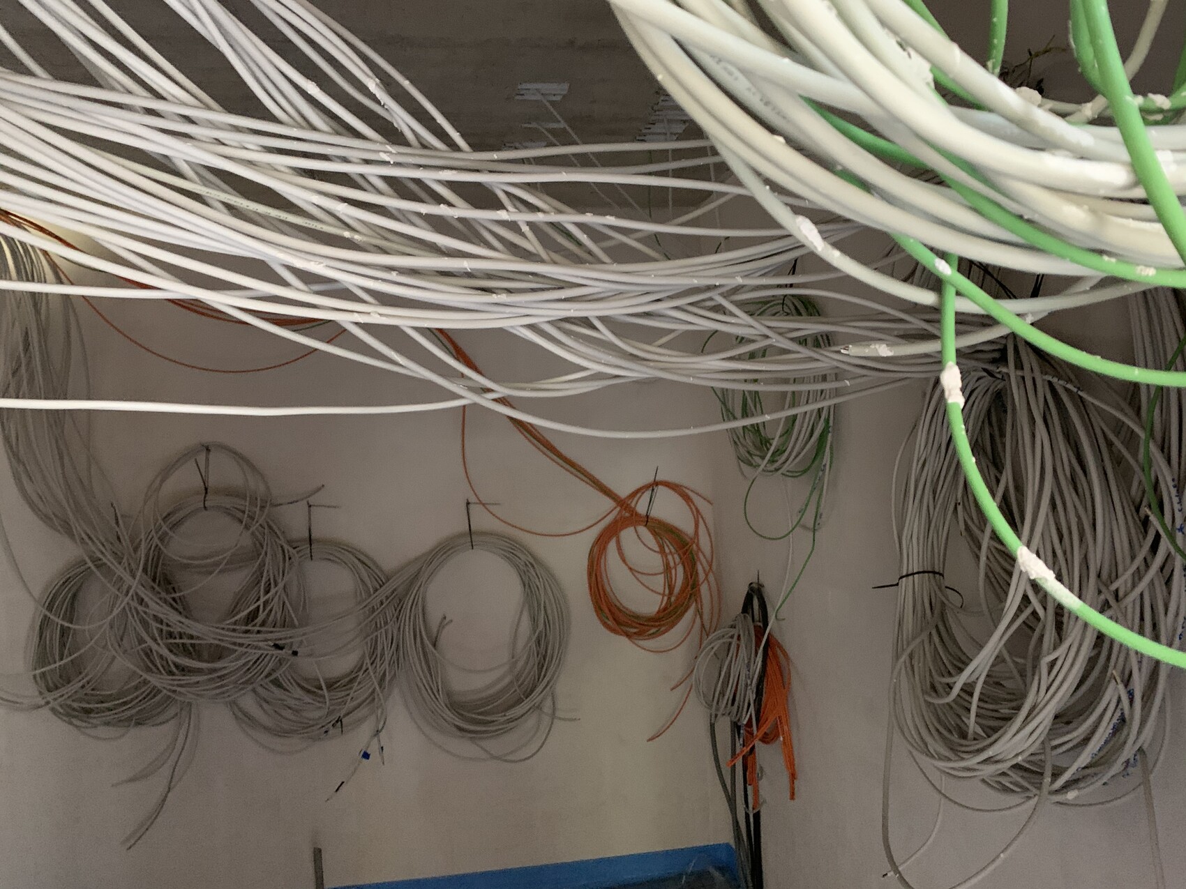 Cable mess of white, gray, and green cables loosely hung on the ceiling and wall.