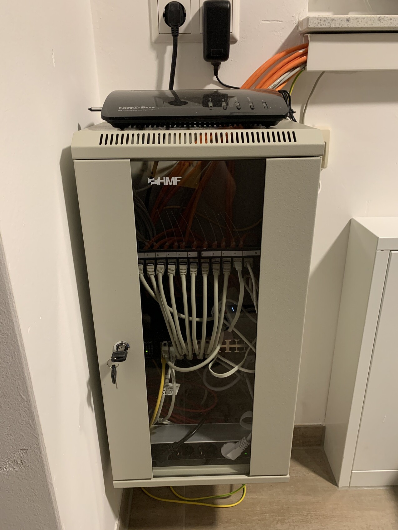 Cable cabinet with FRITZ!Box router on top and patch cables in the glass compartment