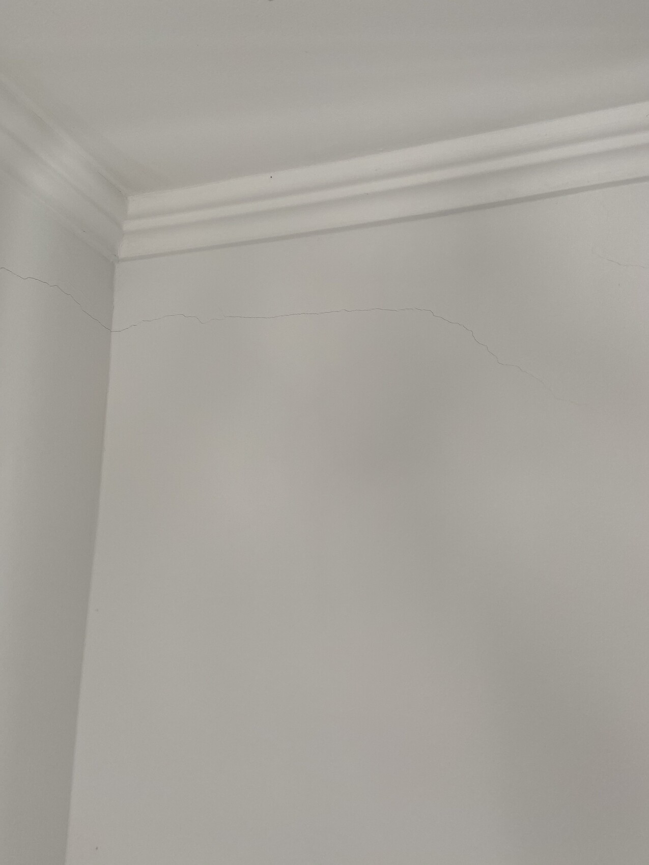 White interior wall corner with fine crack below the ceiling molding.