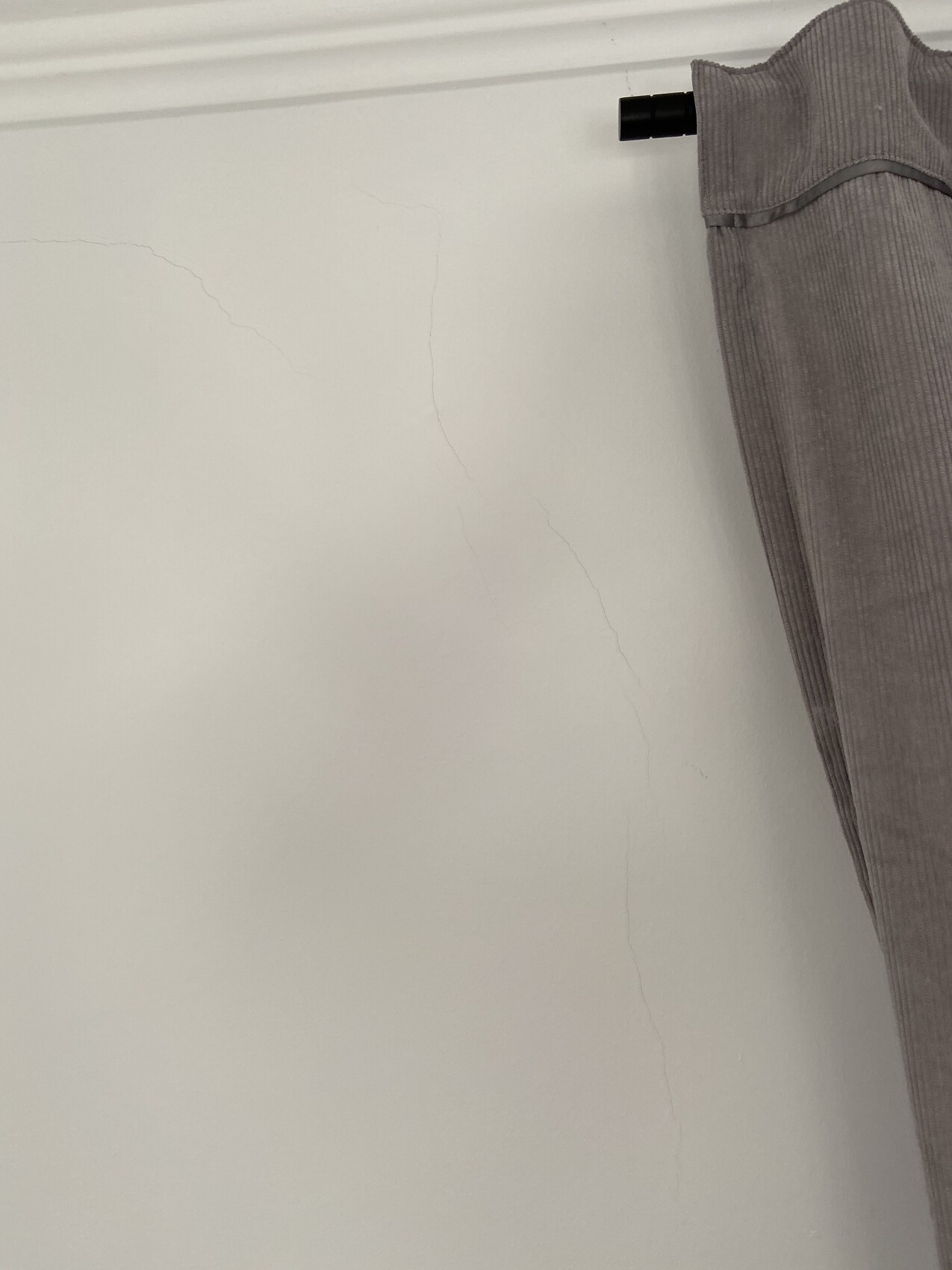 White wall with fine cracks; gray curtain on the right, visible rod above.