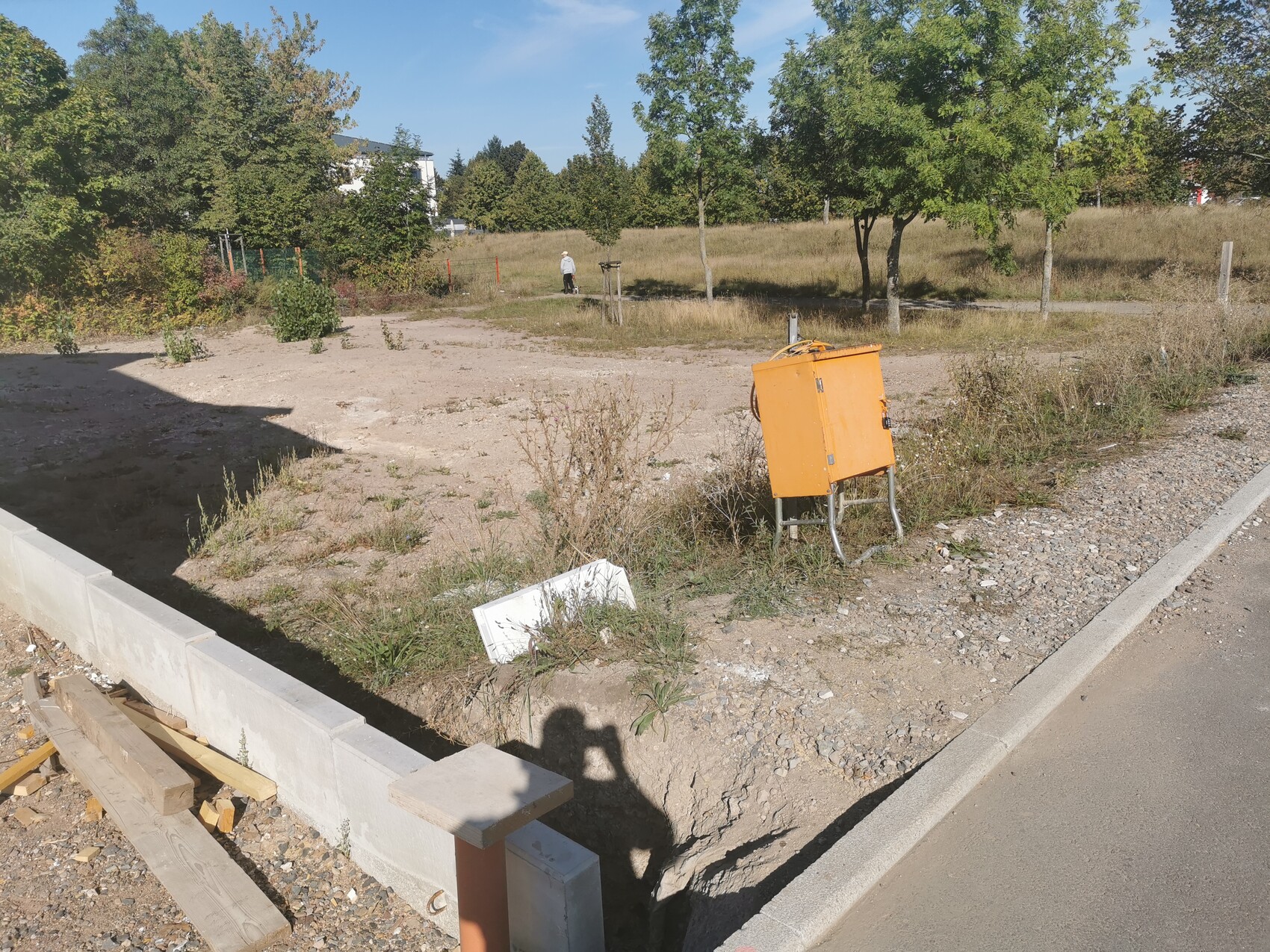 Baustellenbereich mit orangefarbener Werkzeugbox auf Metallgestell, Holzlatten und Kies.