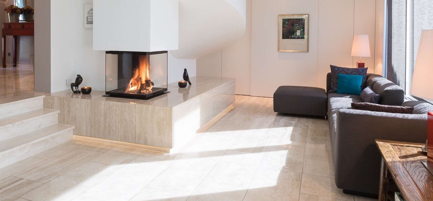 Modern living room with chimney on stone pedestal, gray sofa, and colorful cushions.