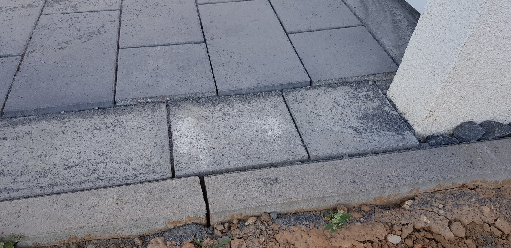 Outdoor area with gray concrete slabs as steps next to a white wall; gravel at the edge.