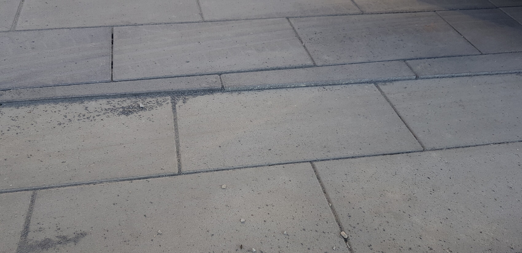 Paved walkway made of gray rectangular slabs; dust and small pebbles on top.