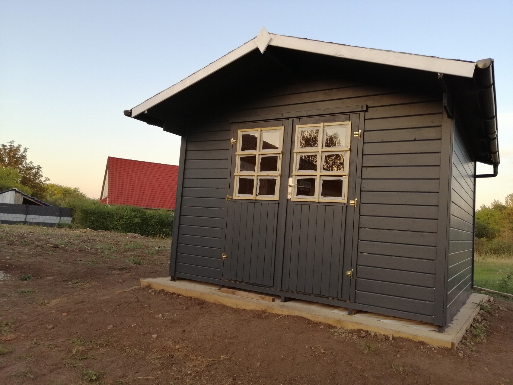 Dark gray wooden cabin with double doors and window front on concrete foundation.