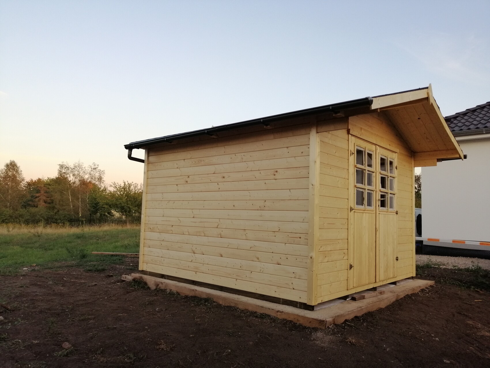 Small natural wood shed with door and window front on wooden foundation outdoors.