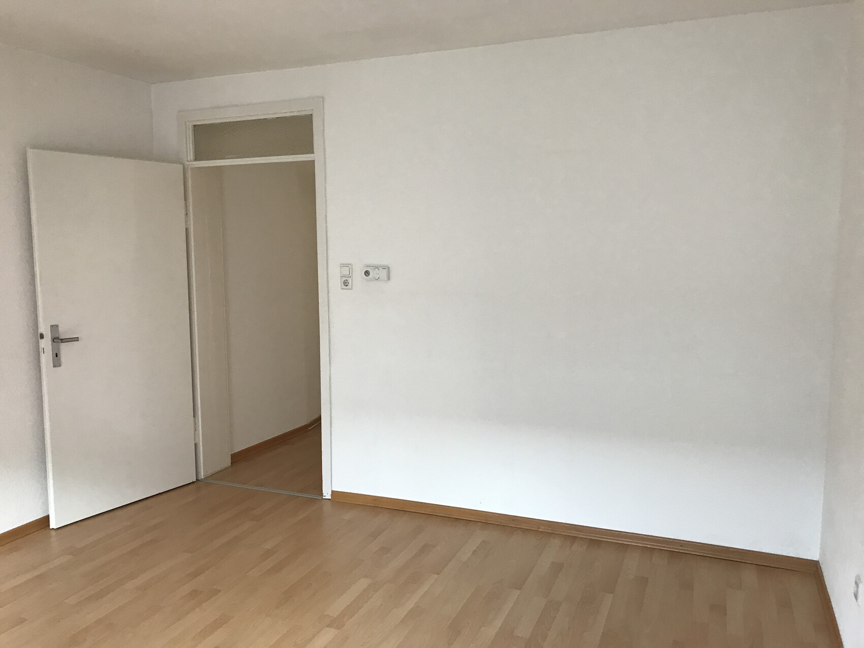 Empty room with light laminate flooring, open door, and white walls.