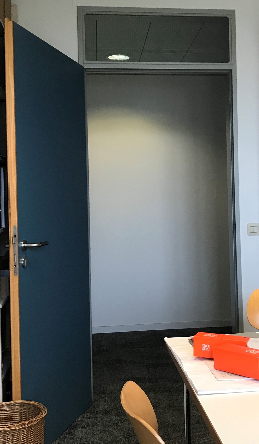 Open blue office door; behind it, an empty corridor with a transom window above the door.