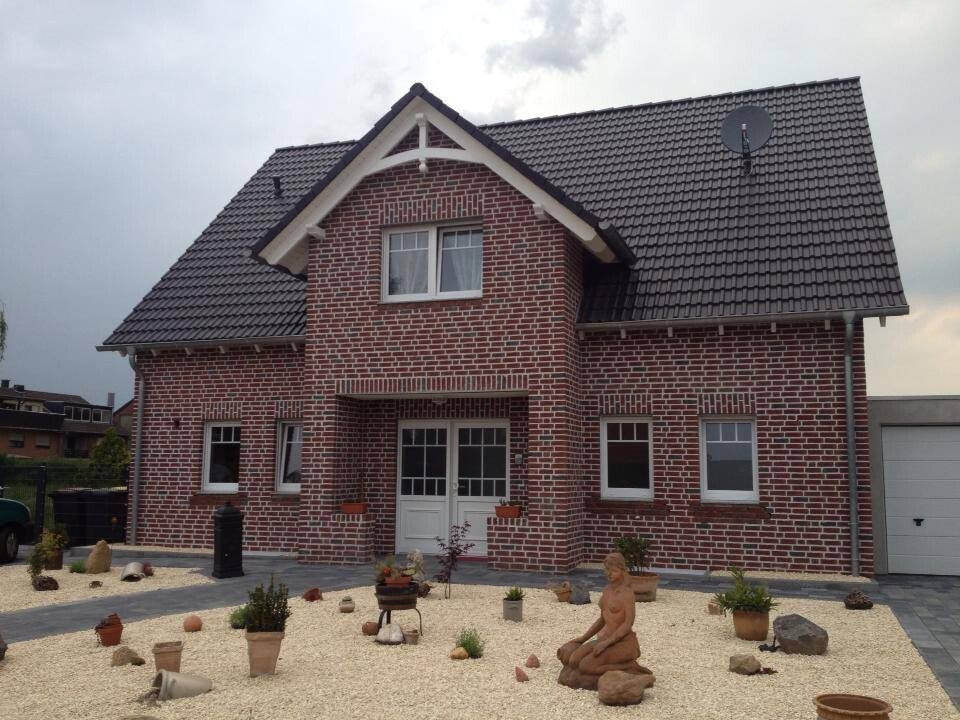 Brick house with dark pitched roof, two stories, gravel garden with potted plants, stone statue and garage.