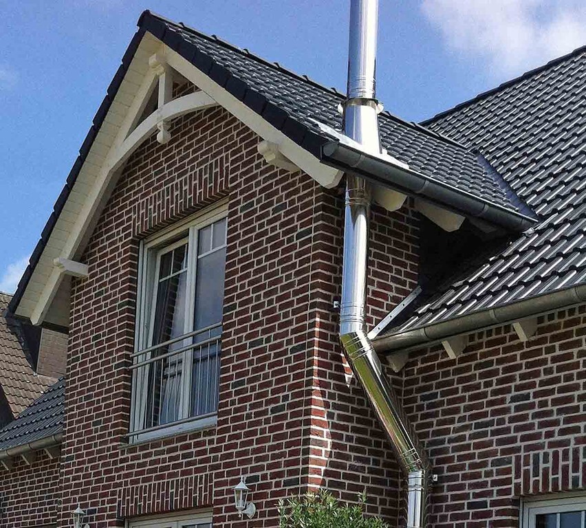 Brick house with dark tile roof, silver gutter and downpipe at the corner