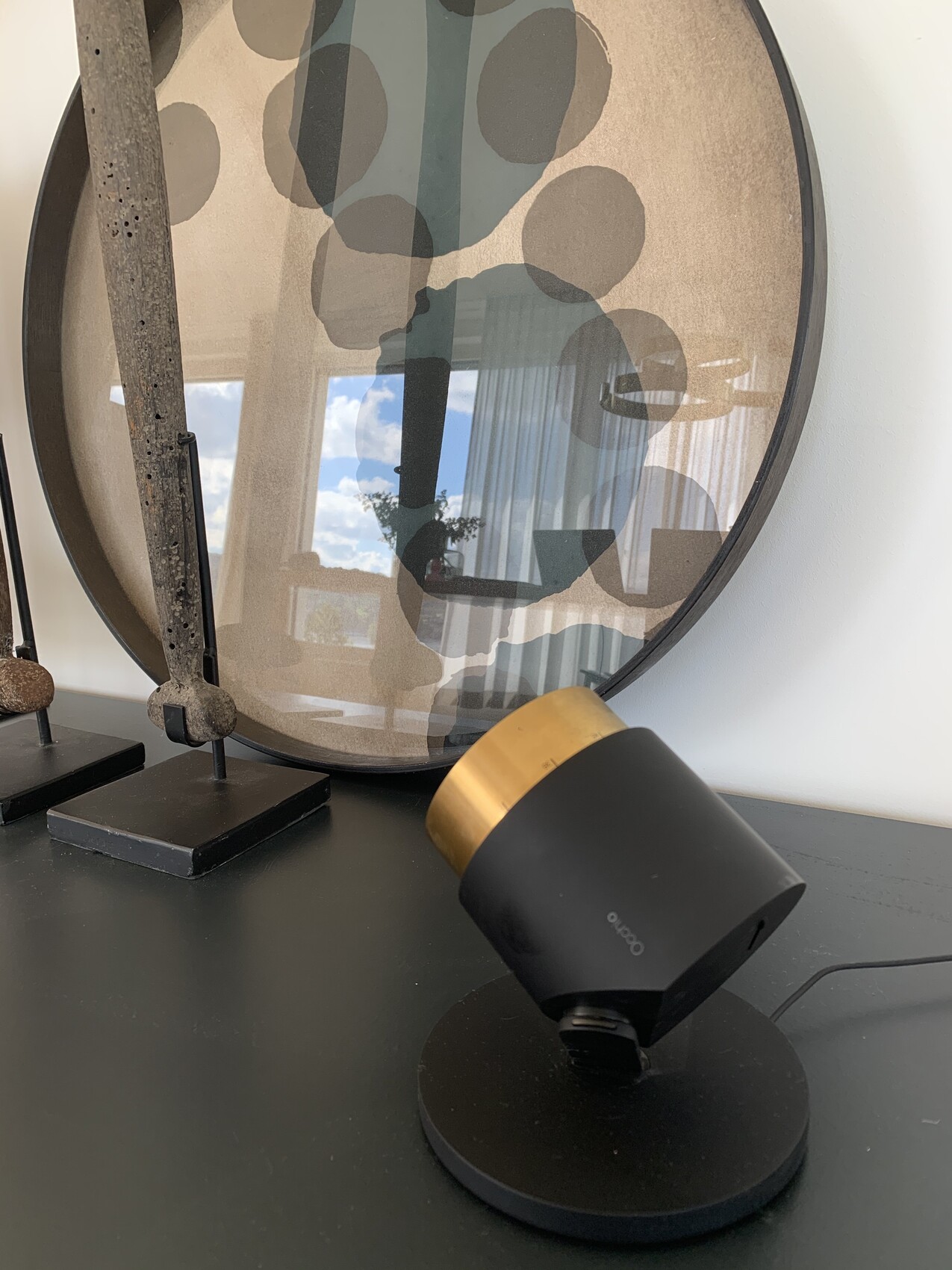 Round mirror with abstract pattern and a black lamp with a golden shade.