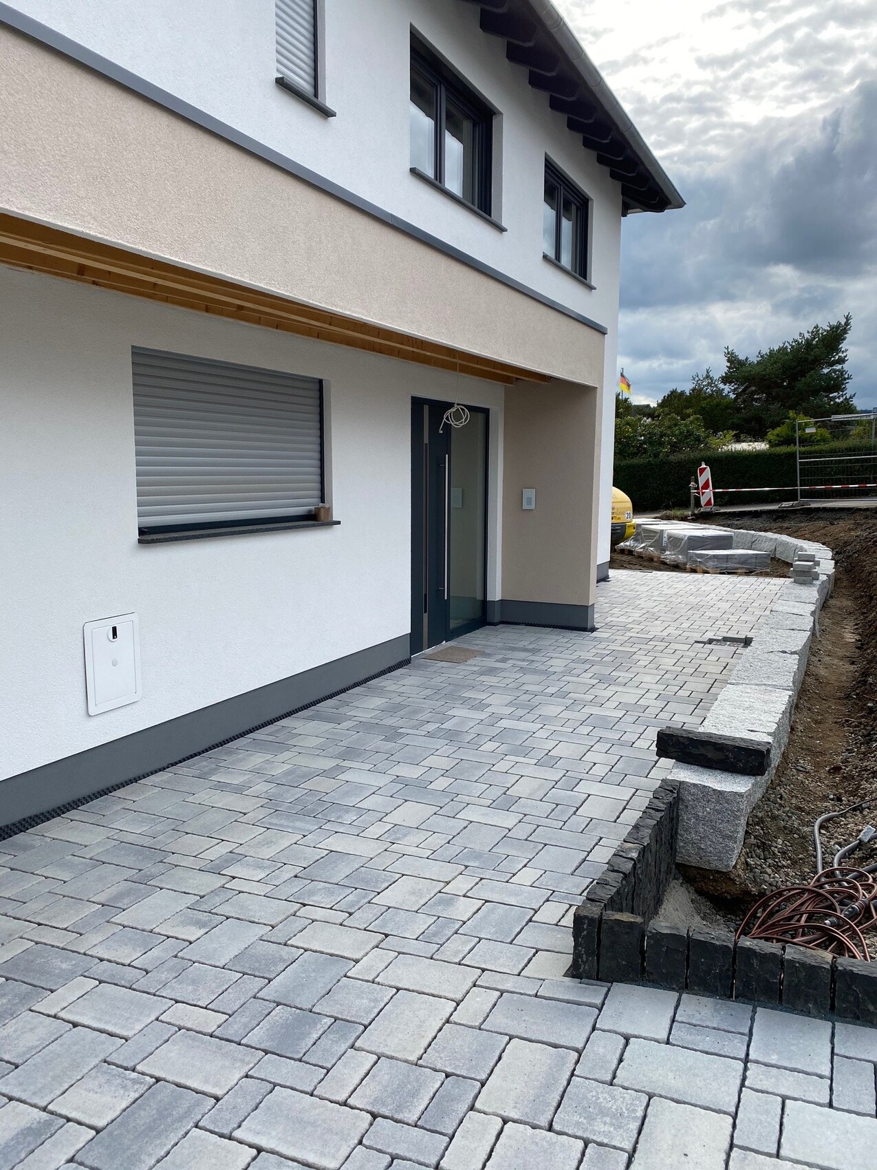 Modern residential complex with paved entrance area; construction work on the right.
