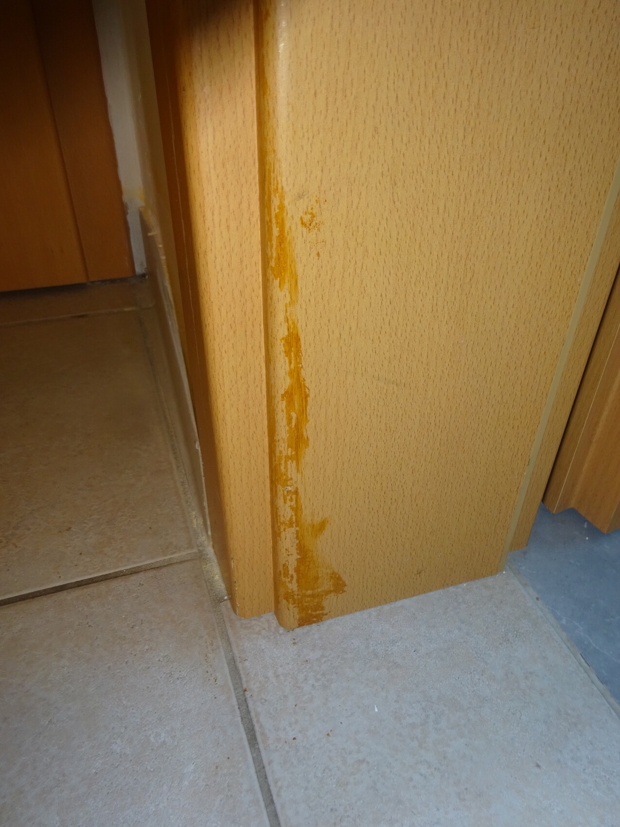 Türrahmen aus Holz mit Lackierung in Orange, die an der Kante abblättert, Bodenfliesen sichtbar.