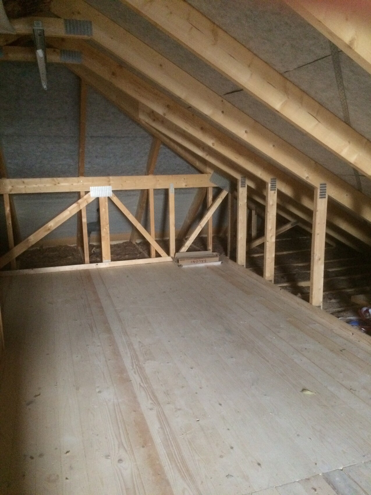 Unplastered attic with visible wooden roof structure and wooden floor.