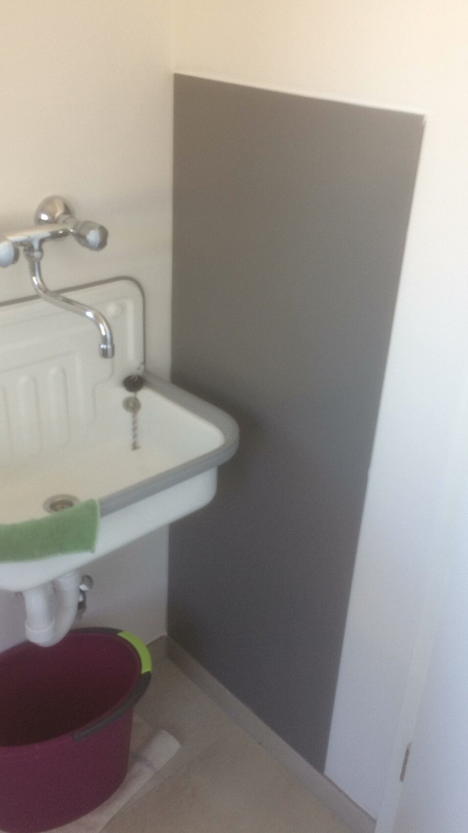 Small utility sink with chrome faucet, gray backsplash panel, pink bucket underneath.