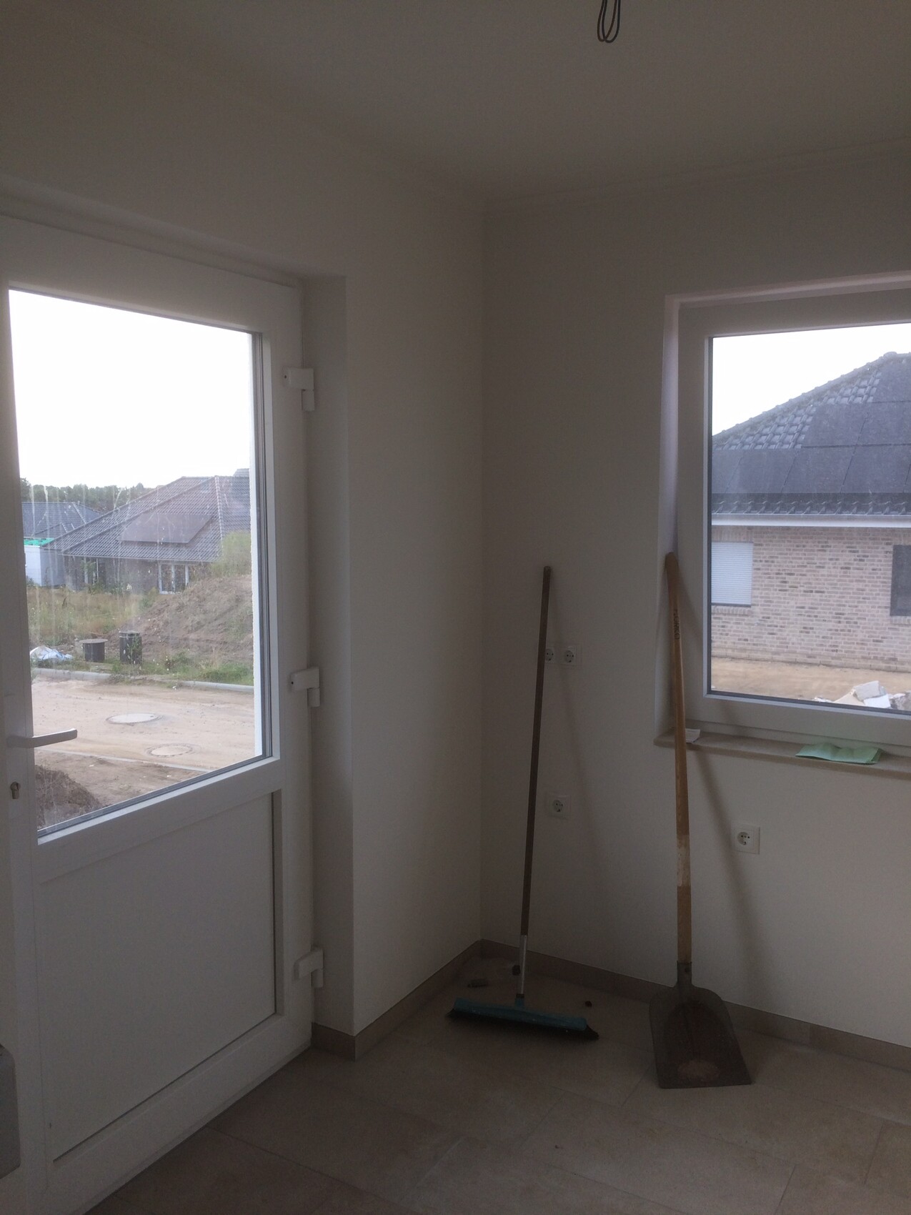 Bright unfinished interior with door and window; broom and dustpan stand in the corner.