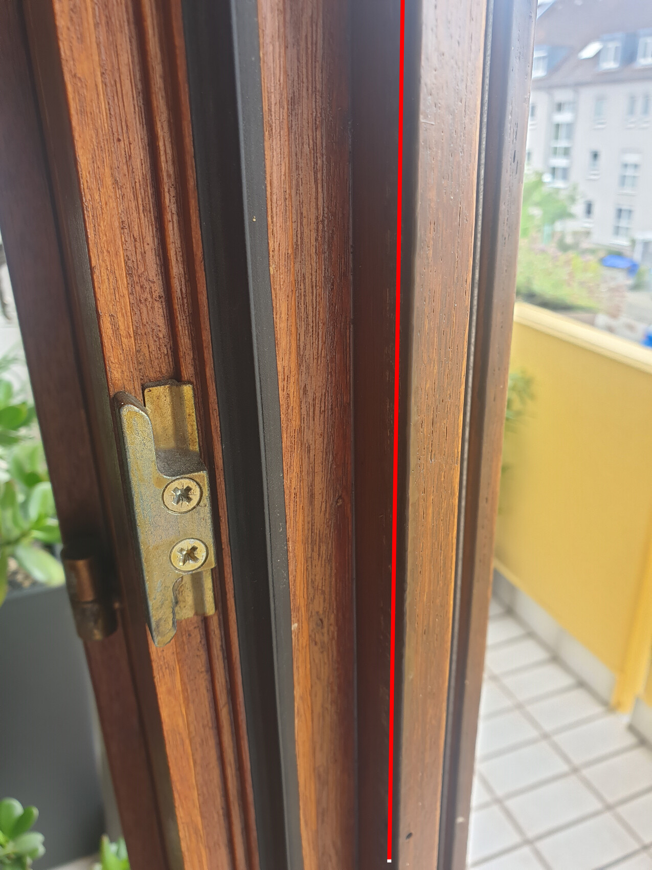 Close-up of a wooden window frame with brass hinge; exterior area with tiles.