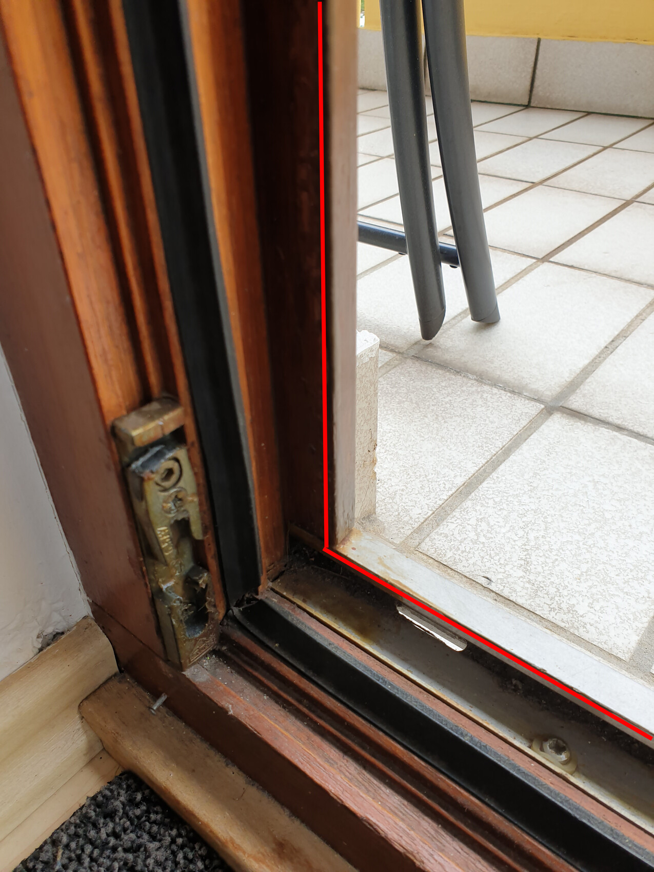Open wooden door with door frame and threshold, tiled floor outside, grey furniture legs visible.