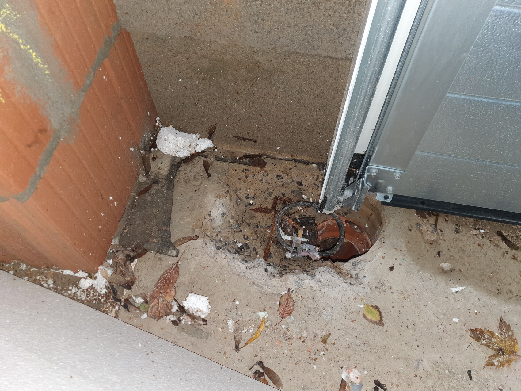 Open round pipe hole in the floor next to the door frame, surrounded by dust and leaves.
