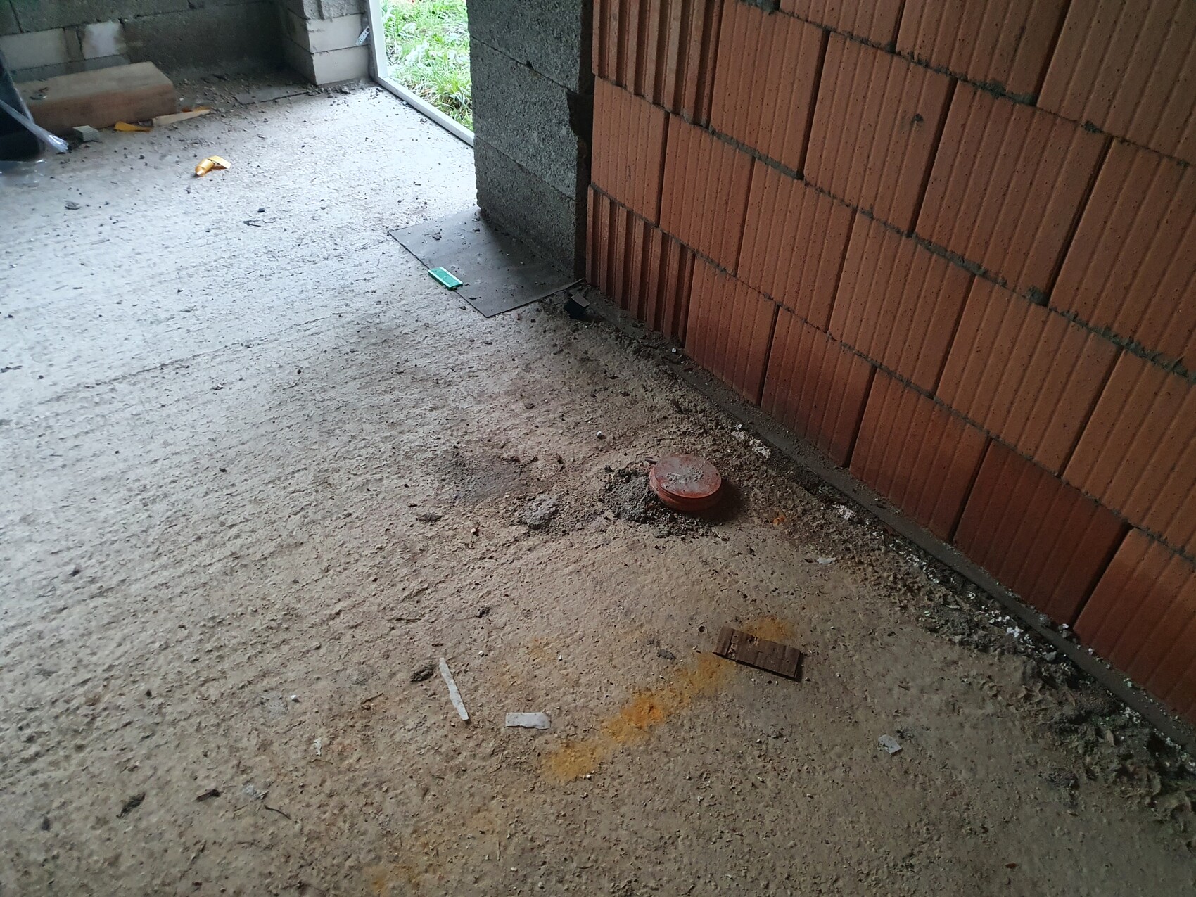 Unfinished interior construction site with a red round cover on a dusty concrete floor next to a red brick wall