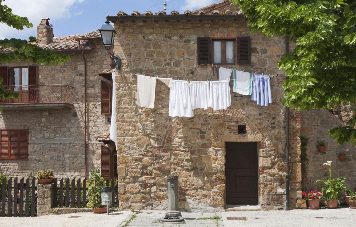 Old stone house made of stone with a clothesline in front in an Italian village, plants and lantern.