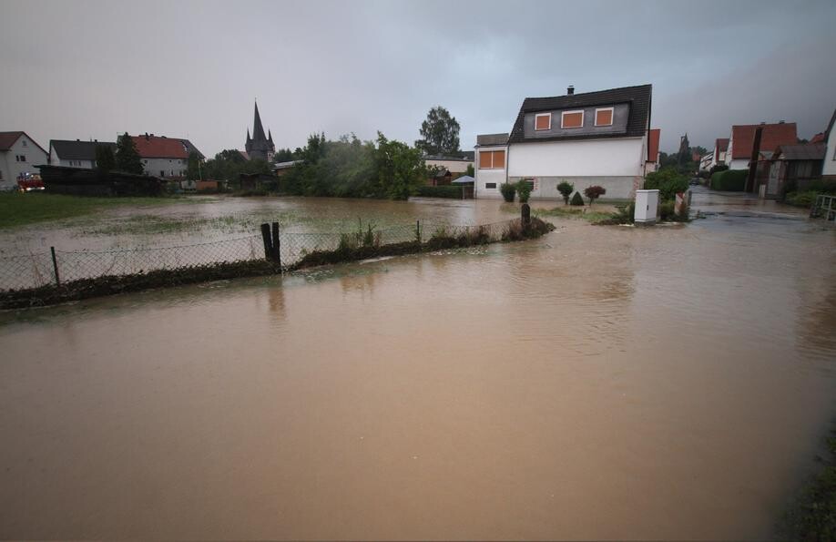 Flooded residential street: houses, garden fence, and water covering street and gardens.