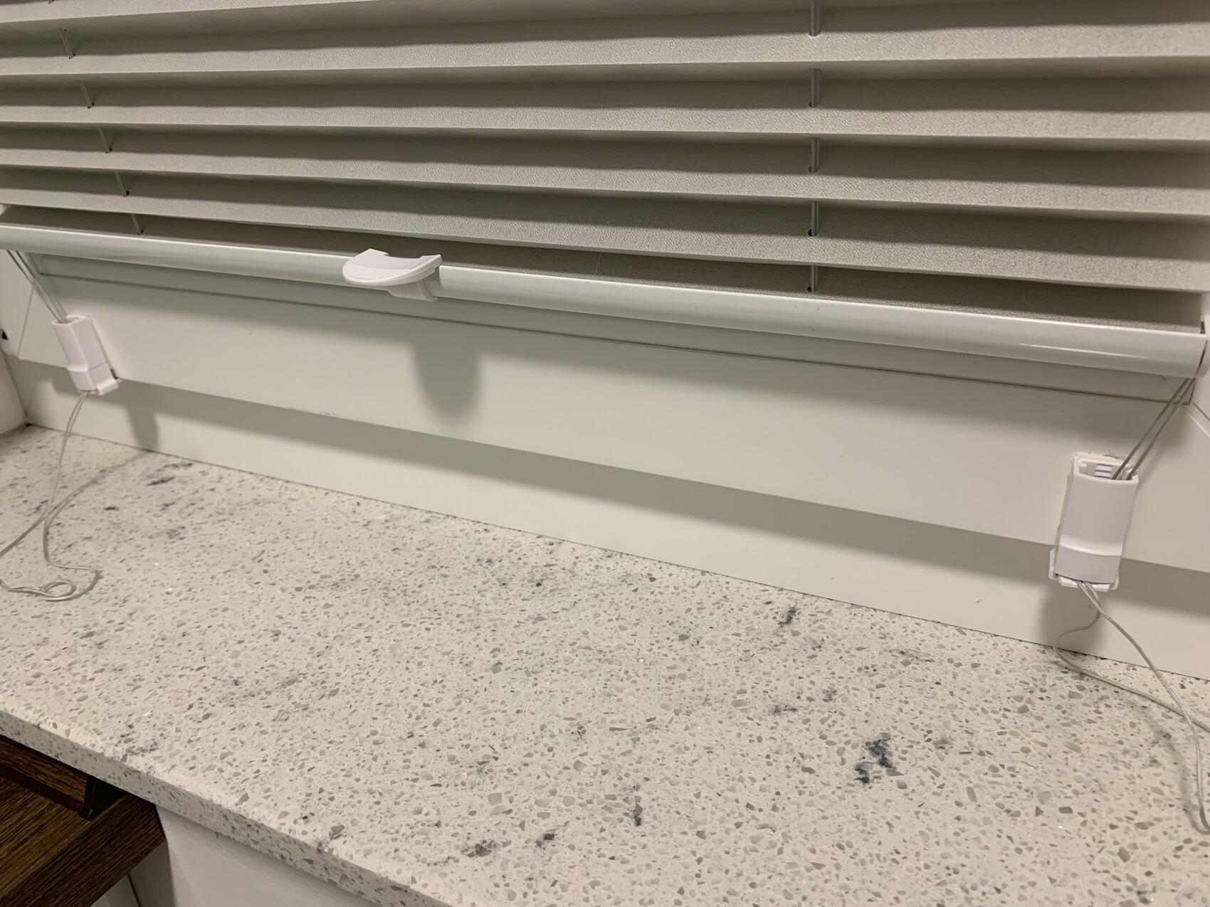Beige horizontal window blinds above a light kitchen countertop; cables lying on the floor.