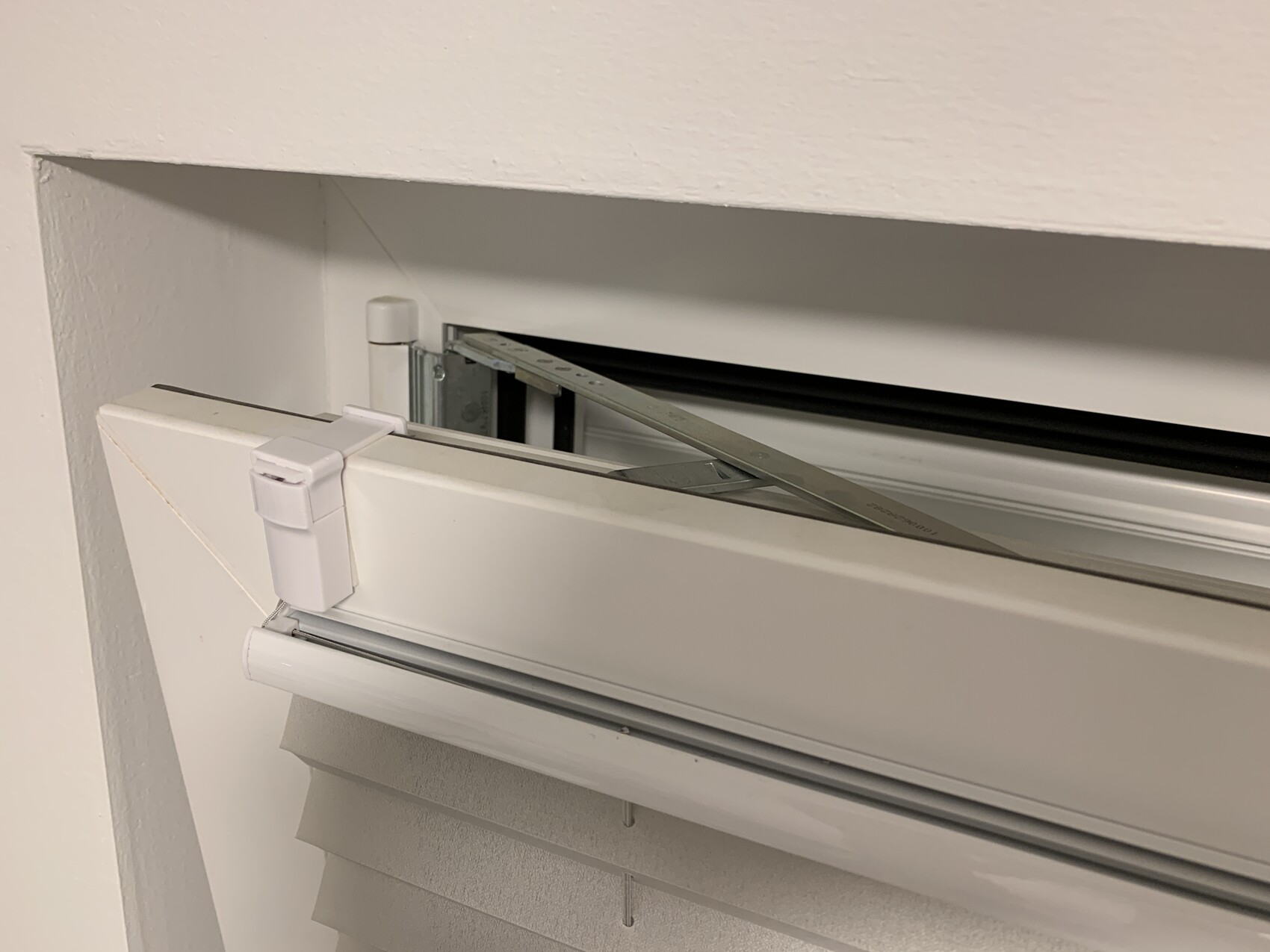 Close-up of a white interior blind with open roller mechanism and metal strip.