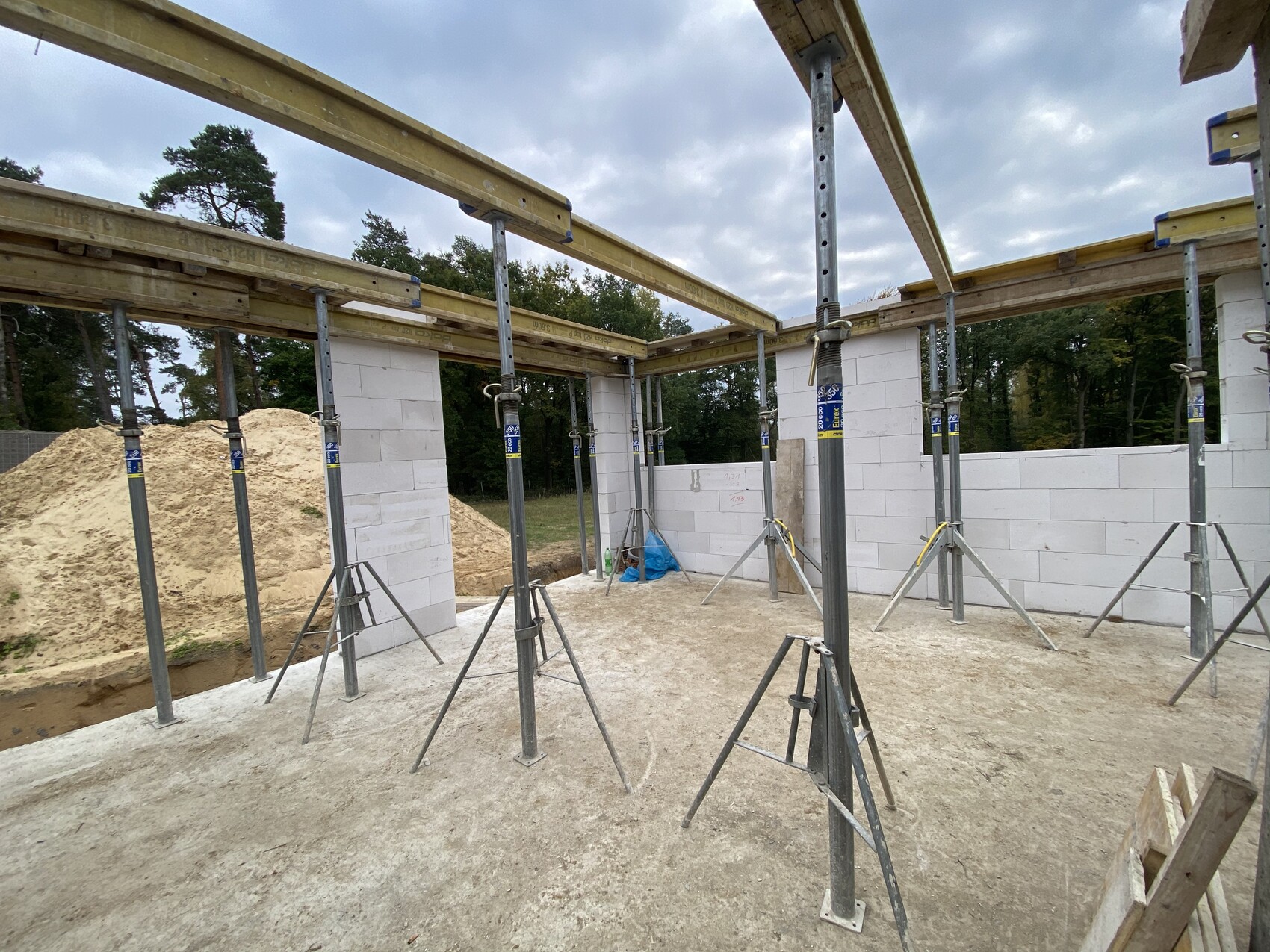 Baustelle: Innenraum mit weißen Betonsteinwänden, Gerüststützen, Holzbalken und Sandhaufen.