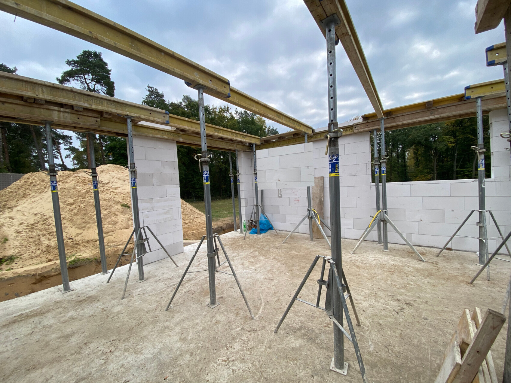 Baustelle mit weißen Blöcken als Wände, Stahlstützen, Holzbohlen und Sandhügel.