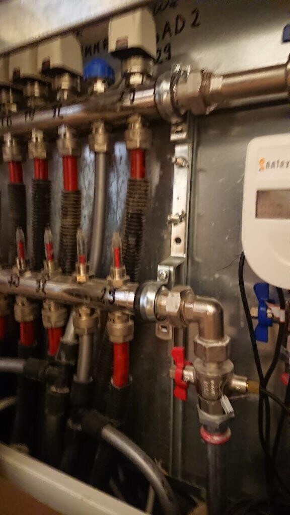 Industrial installation with metal pipes, red hoses, valves, and measuring device.