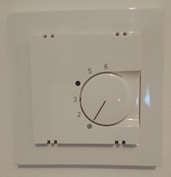 White thermostat rotary knob on the wall with scale 2–6; pointer roughly on 4.