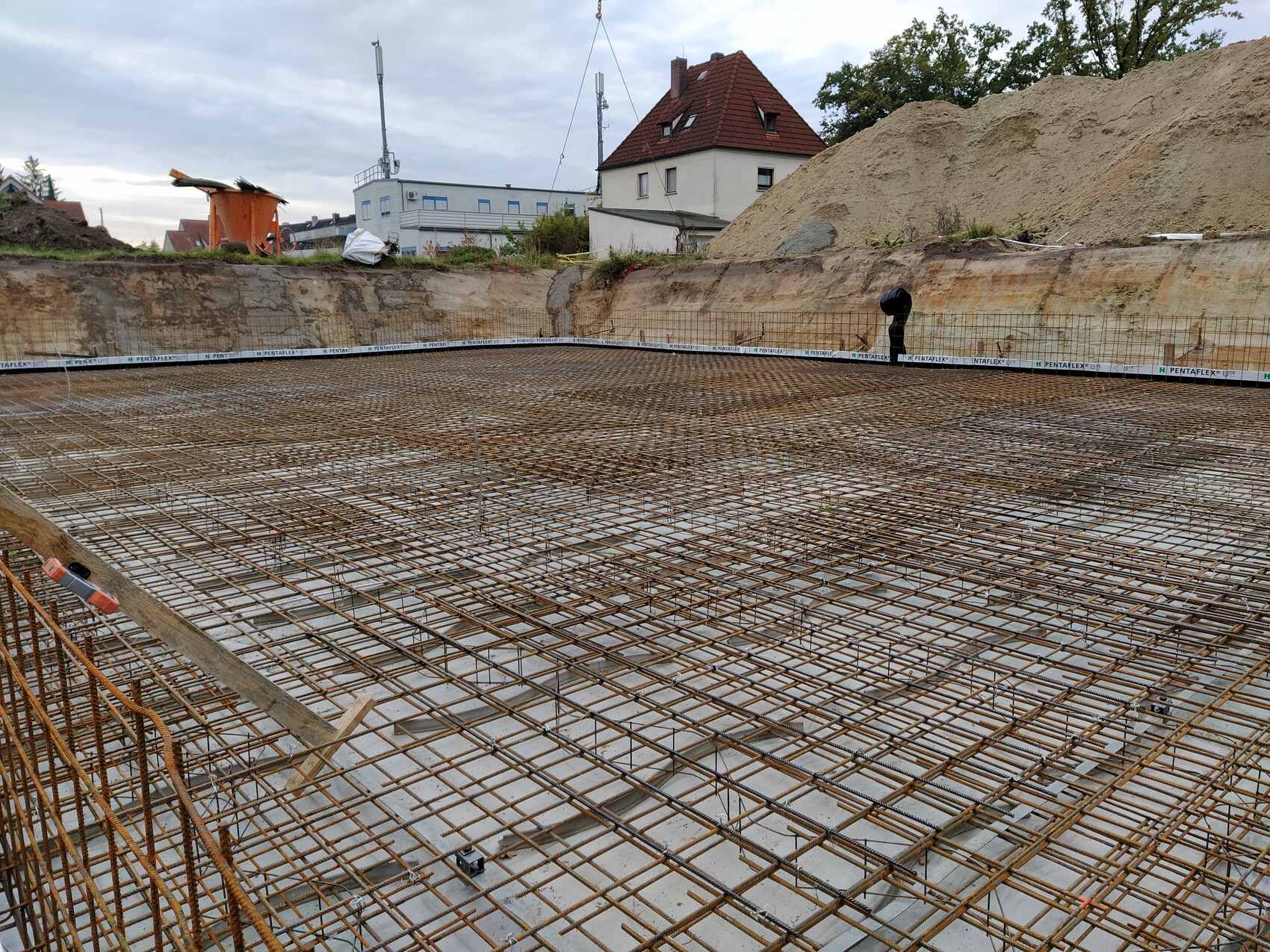 Bewehrungsstahlgitter ueber Fundament, Baustelle, Arbeiter am Rand, Erdwall dahinter.