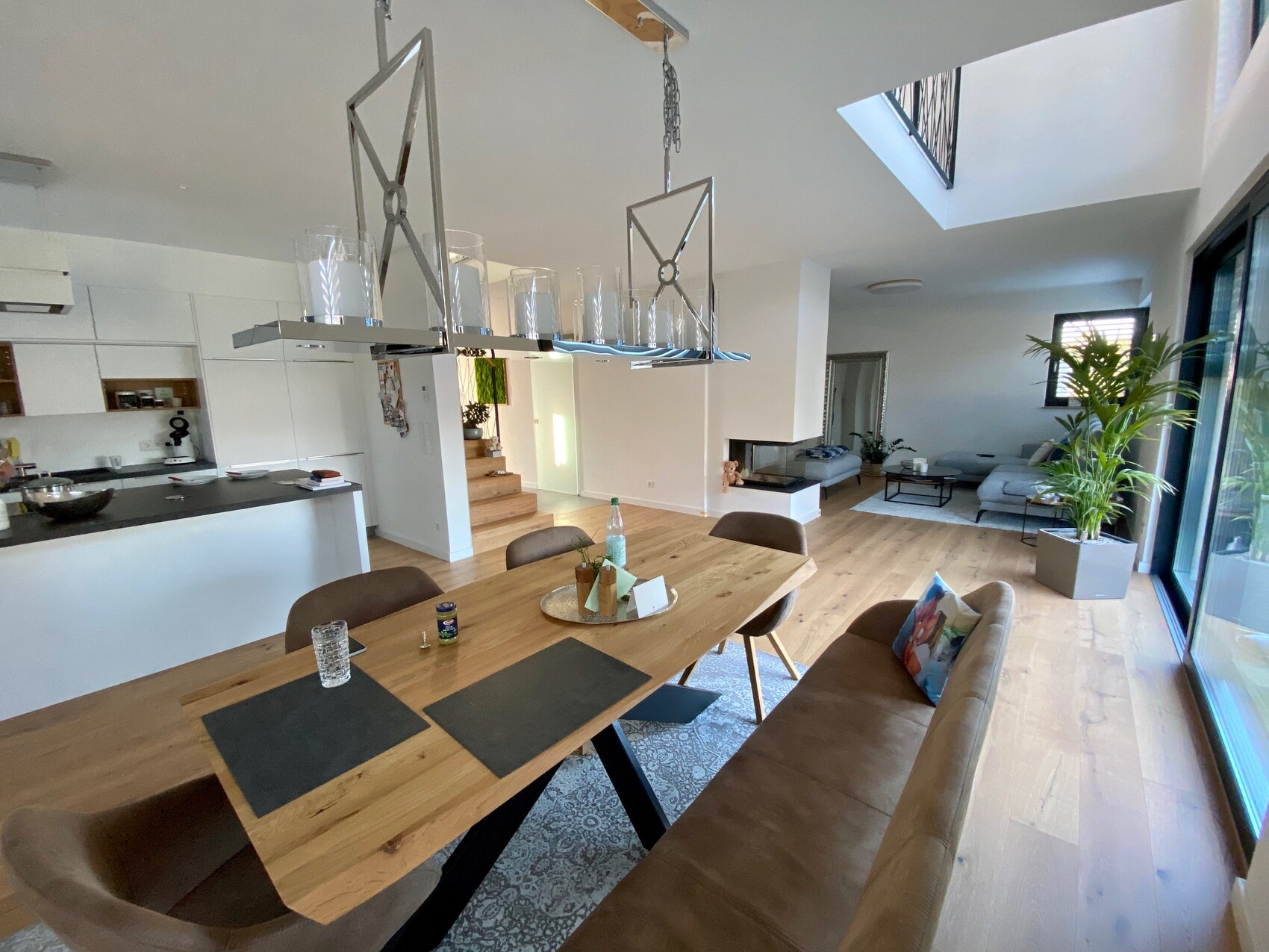 Open living and dining area: wooden table, chairs, kitchen on the left, sofa, and plant.