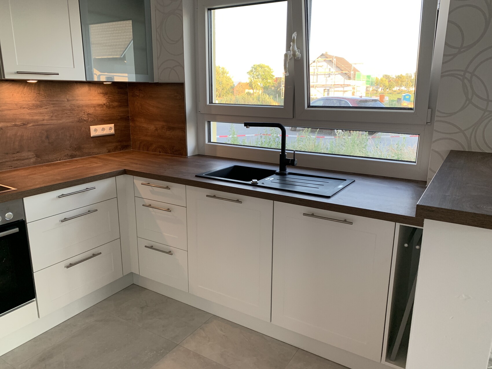 Modern L-shaped kitchen with white cabinets, brown wood countertop, sink under the window.