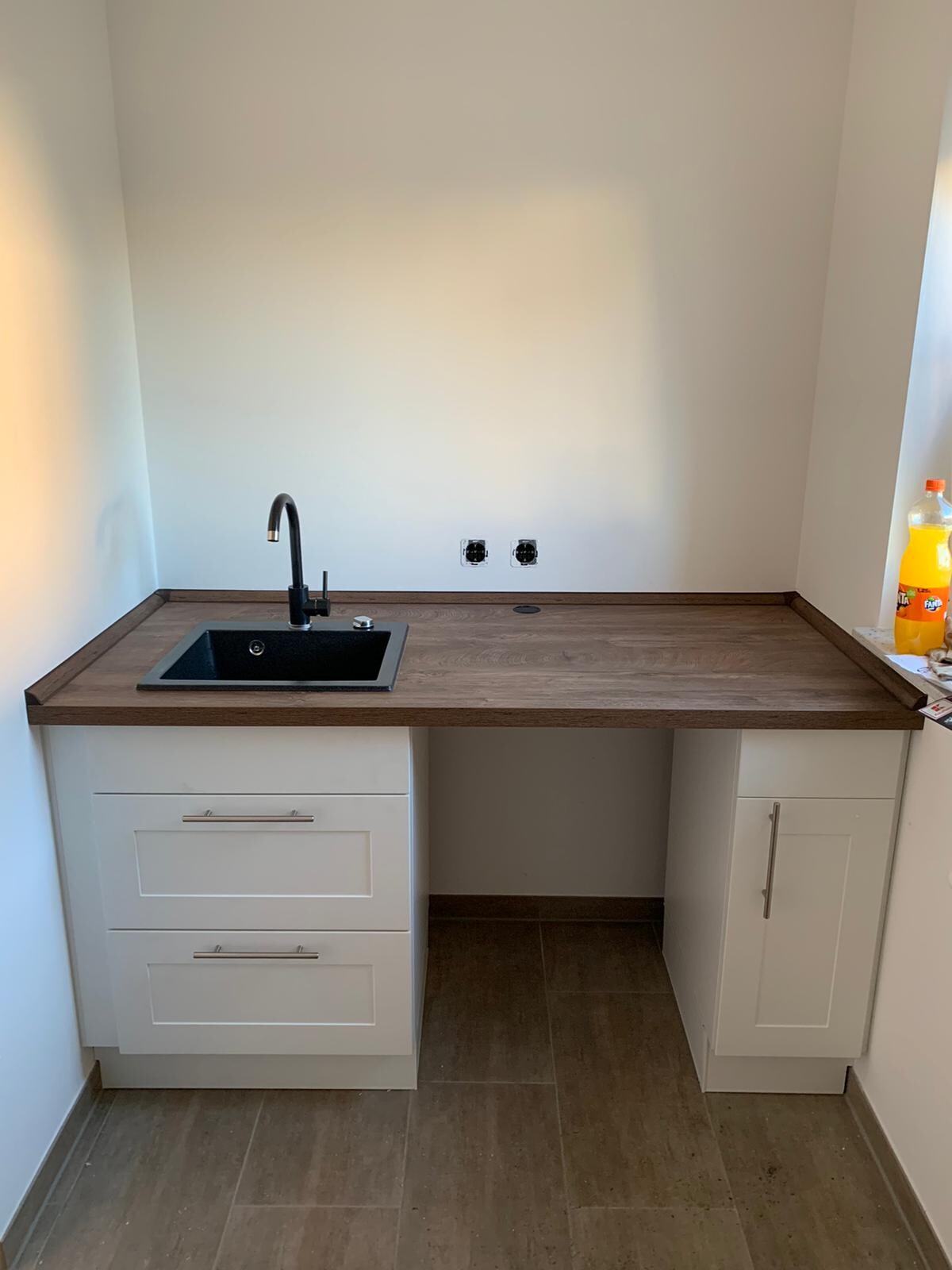 Kitchen: dark wood countertop, black sink, faucet, and white base cabinets; bottle on the right.