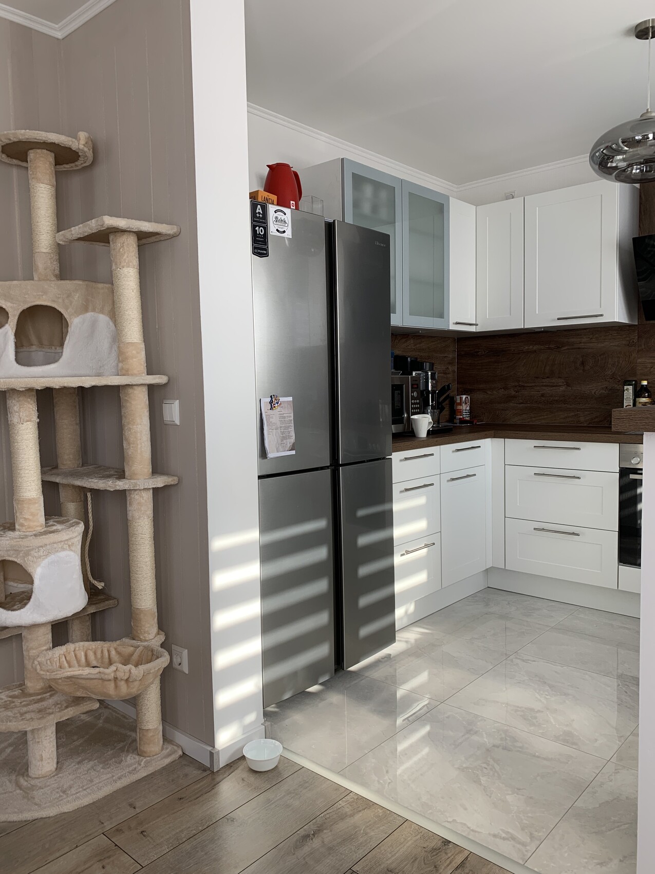 Modern kitchen with stainless steel refrigerator, white cabinets, and cat tree on the left.