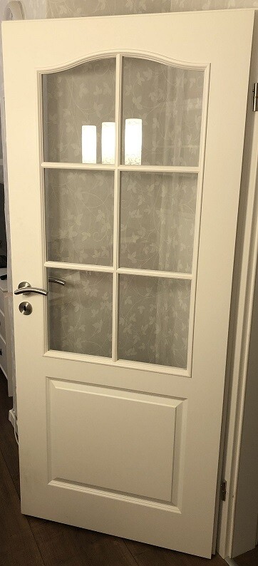 White interior door with six glass windows in a grid frame; door handle on the left.
