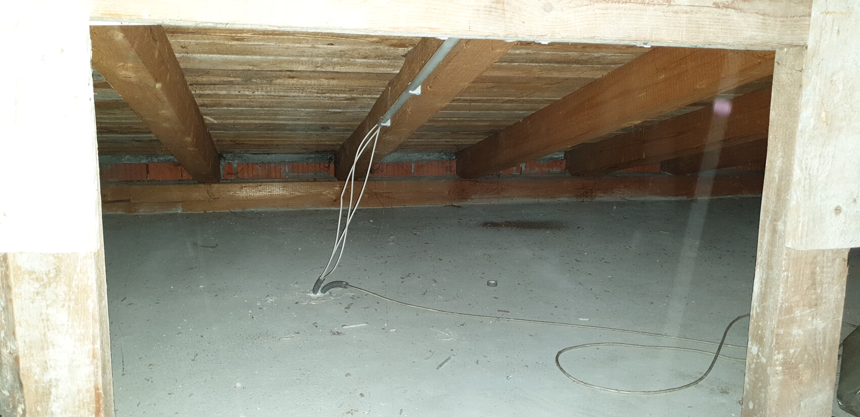Basement/attic with wooden beam ceiling; loose cables hanging over dusty concrete floor