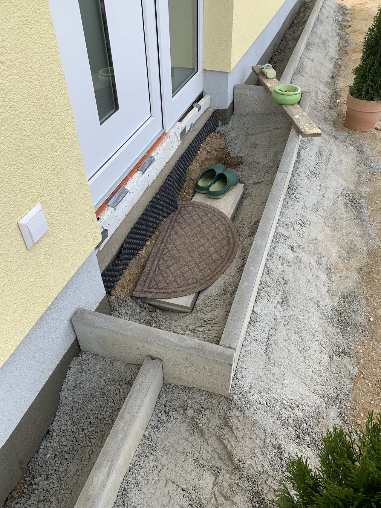 Construction work on the house: open trench at the foundation, green house slippers, brown cover, potted plants