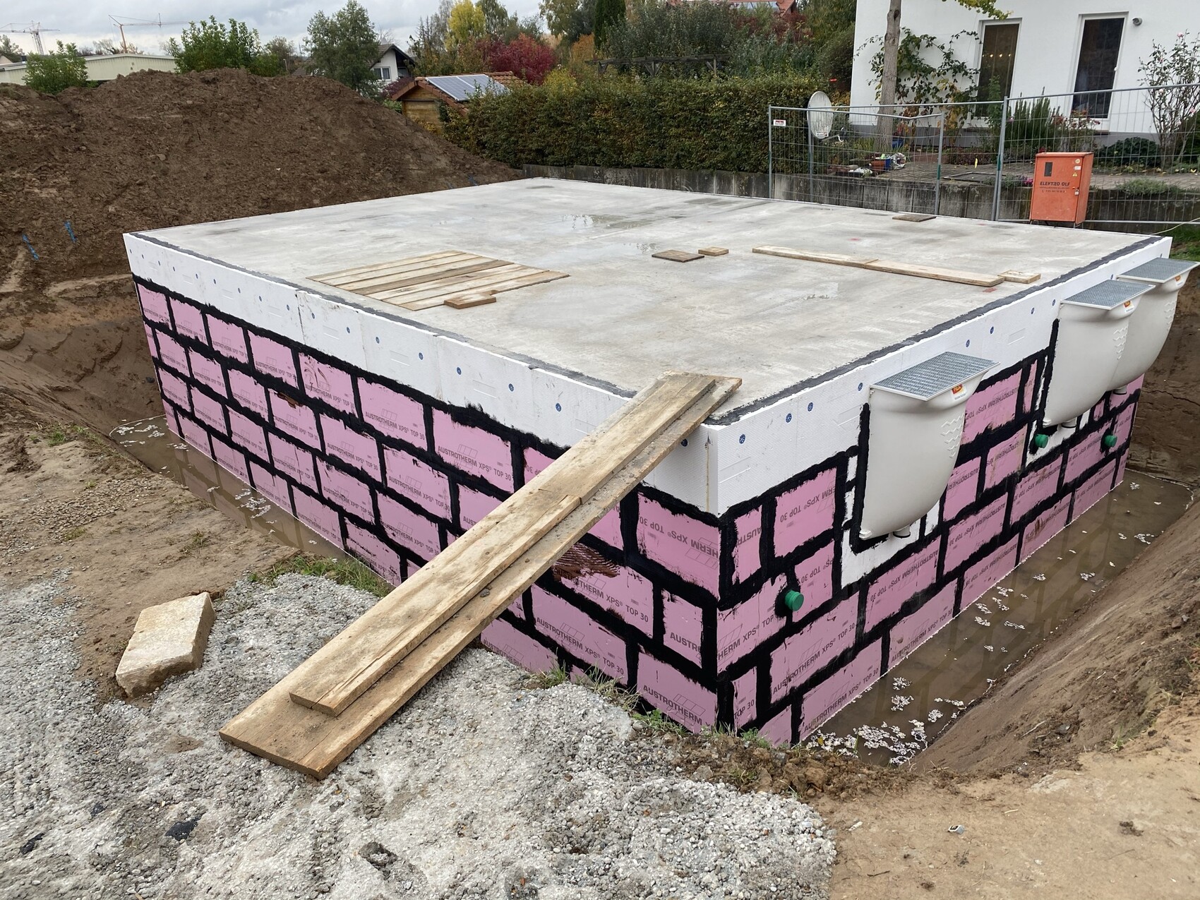 Concrete foundation of a building with pink insulation, black joints, wooden planks, and pipes.