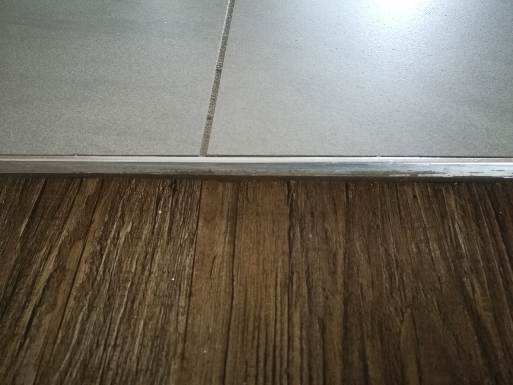 Door threshold: transition from gray tiles to wood-colored flooring with metal edge.