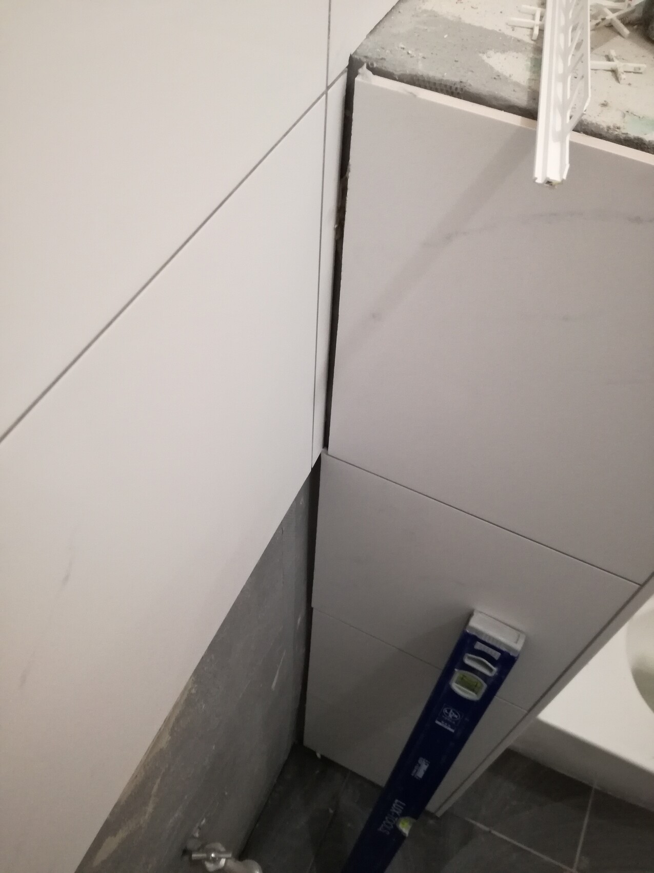 Bathroom construction site: white wall and floor tiles, a blue spirit level leaning against the tiles.
